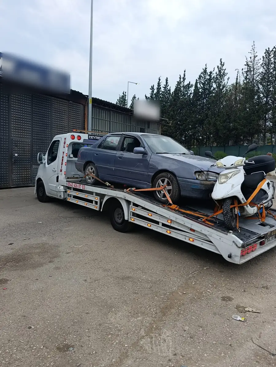 Beyaz çekicinin platformunda kayışlarla bağlanmış mavi bir otomobil ve bir motosiklet