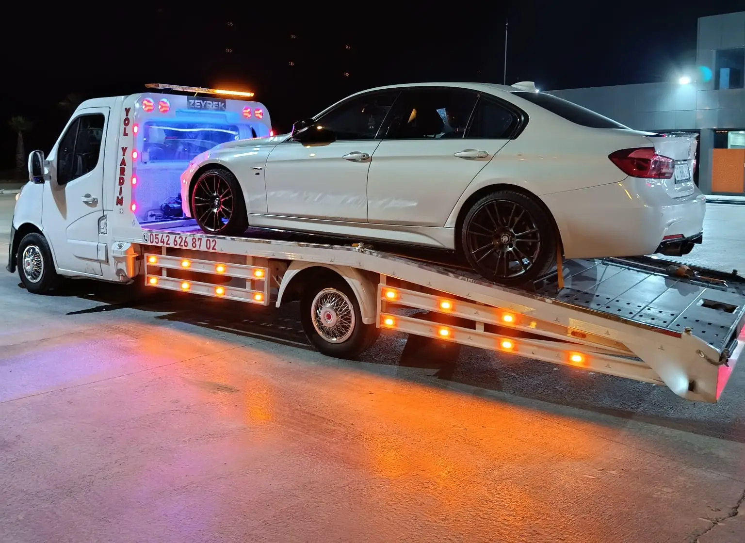 Lara için gece Zeyrek Oto Çekici’nin platformlu çekicisi beyaz bir sedan otomobili sarı uyarı lambalarıyla taşıyor